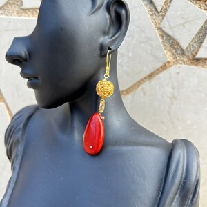 May include: Gold and red dangle earrings with a wire ball and a teardrop-shaped red stone.