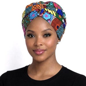 May include: A colorful turban with a patchwork design featuring various patterns and colors, including orange, blue, green, and pink. The head covering is worn by a person wearing a black shirt.