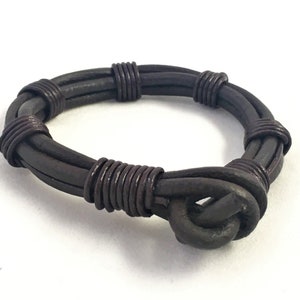 May include: A brown leather bracelet with a wire wrapped around it. The bracelet has a knot on one end.