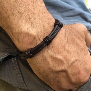 May include: A brown leather bracelet with multiple strands woven together. The bracelet is tied with a knot on the wrist.
