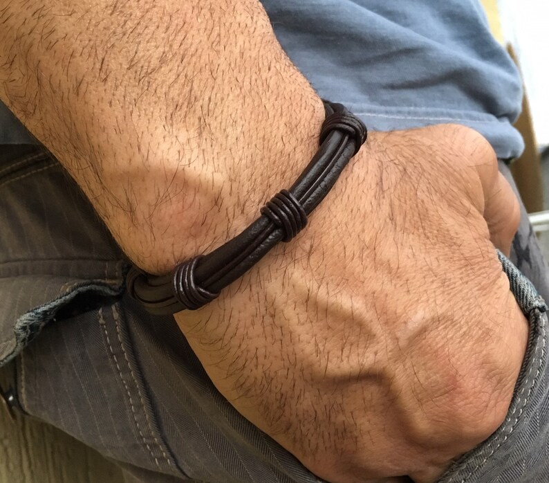 May include: A brown leather bracelet with multiple strands woven together. The bracelet is tied with a knot on the wrist.