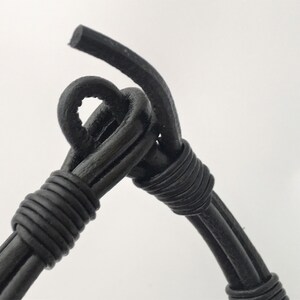 May include: Close-up of a black leather bracelet with a knotted design. The bracelet is made of multiple strands of leather that are woven together.