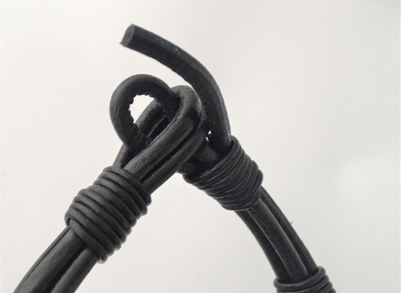 May include: Close-up of a black leather bracelet with a knotted design. The bracelet is made of multiple strands of leather that are woven together.