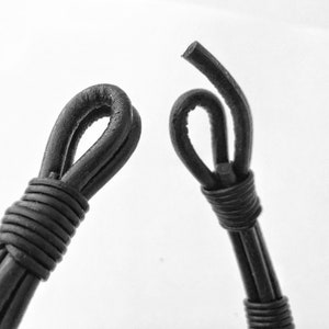 May include: Two black leather cord ends with loops, one is tied in a knot, the other is a simple loop.