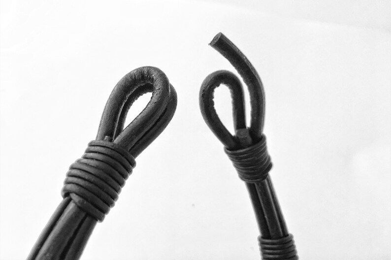May include: Two black leather cord ends with loops, one is tied in a knot, the other is a simple loop.