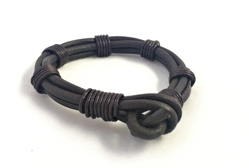 May include: A brown leather bracelet with a wire wrapped around it. The bracelet has a knot on one end.