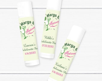 Peut inclure: Trois tubes de baume à lèvres avec des étiquettes personnalisées. Les étiquettes présentent un graphisme de verre à margarita avec le texte "Margs & Matrimony" et des noms avec des dates. Le fond est jaune clair.