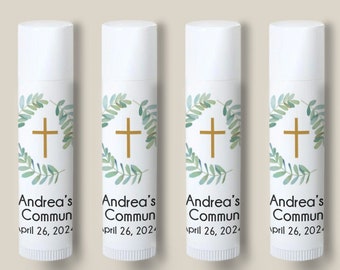May include: Five white lip balm tubes with labels featuring a gold cross, green leaf design, and the text "Andrea's Communion April 26, 202-". The tubes are arranged in a row against a neutral background.