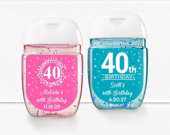 May include: Two clear plastic bottles of hand sanitizer with personalized labels. The labels are pink and blue with white text and a white number 40. The pink label says "Melissa's 40th Birthday 11.16.28" and the blue label says "Scott's 40th Birthday 6.20.27".