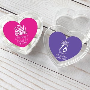 Könnte beinhalten: Zwei transparente herzförmige Plastikbehälter mit Deckeln. Jeder Behälter hat einen bunten Aufkleber mit dem Text "Sweet Sixteen" und personalisierten Details. Der rosa Aufkleber sagt "Mallory's Sweet 16! 7-11-29". Der lila Aufkleber sagt "Sweet 16 Tonette's 16th Birthday June 23, 2025".