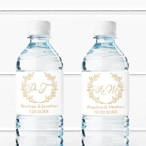 May include: Two clear plastic water bottles with personalized labels. The labels are white with gold lettering and a gold wreath design. The labels include the couples' names and wedding date. The first label reads "P & T Penelope & Jonathan 1.25.20XX". The second label reads "A & M Angelina & Matthew 10.22.20XX".