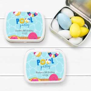 May include: Two white rectangular tins with blue and white pool party designs. The tins have a blue background with white polka dots and a pool with a yellow and red float, a blue and white float, and a beach ball. The text "Pool party" is in blue and white letters. The top tin has the text "Scarlett's 8th Birthday 5.3.27" and the bottom tin has the text "Madison's 5th Birthday 6.9.26".