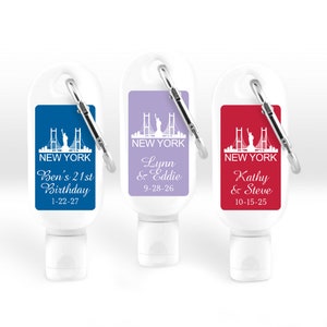 May include: Three clear plastic bottles with a carabiner clip. Each bottle has a different colored label with a white silhouette of the New York City skyline, including the Statue of Liberty and the Brooklyn Bridge. The labels also include personalized text, such as "Ben's 21st Birthday 1-22-27", "Lynn & Eddie 9-28-26", and "Kathy & Steve 10-15-25".
