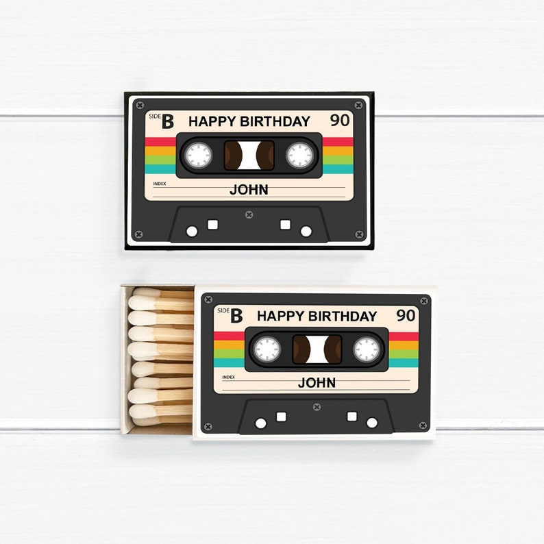 May include: Two matchboxes with a retro cassette tape design. The cassette tapes are black with a colorful stripe and the text "HAPPY BIRTHDAY 90" and "JOHN". One box is open, revealing wooden matches.