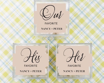 Peut inclure: Trois boîtes en verre transparent remplies de bonbons blancs. Chaque boîte porte une étiquette beige avec du texte noir. La boîte du haut indique "Notre favori Nancy + Peter". La boîte de gauche indique "Son favori Nancy + Peter". La boîte de droite indique "Son favori Nancy + Peter".