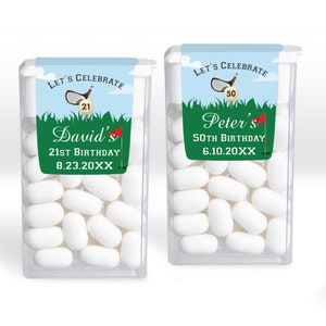 May include: Two clear plastic containers of mints with personalized labels. The labels are green, blue, and white with a golf club and ball design. The text on the labels reads "Let's Celebrate" and includes the name, age, and date of the birthday. The first label reads "David's 21st Birthday 8.23.20XX". The second label reads "Peter's 50th Birthday 6.10.20XX".