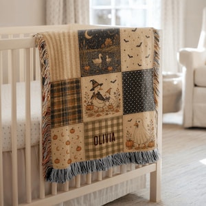 May include: A woven throw blanket featuring a patchwork design with Halloween-themed illustrations including ducks in costumes, pumpkins, bats, and moons. The blanket includes the name OLIVIA in a dark font and has a fringed edge with multi-coloured threads.