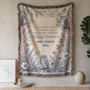 Puede incluir: Una manta tejida beige con un diseño floral y de búhos azul marino. La manta tiene el texto "YOU CHANGED LIVES EVERY SINGLE DAY AND THAT WILL NEVER FADE Happy Retirement MRS. BAKER 2026."