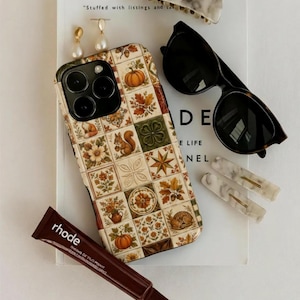 Puede incluir: Un surtido de accesorios que incluyen una funda de teléfono estampada, gafas de sol, pinzas para el pelo, pendientes y un tubo de bálsamo labial. La funda del teléfono presenta un patrón repetido de calabazas, flores y ardillas. Las gafas de sol tienen montura carey.