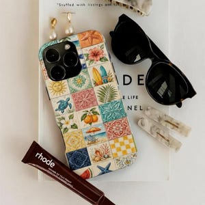 Puede incluir: Un surtido de accesorios que incluyen una funda de teléfono con un diseño de azulejos coloridos, gafas de sol, pinzas para el pelo, pendientes y un tubo de producto labial. La funda del teléfono presenta ilustraciones con temática de playa.