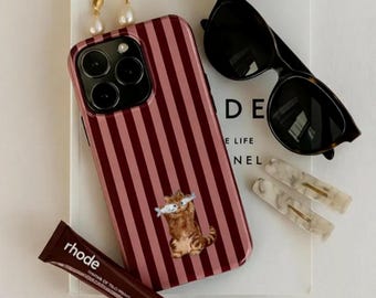 Op de afbeelding: Een verzameling accessoires, waaronder een telefoonhoesje, zonnebril, haarclips en oorbellen. De telefoonhoes is roze met verticale bordeauxrode strepen en een kattenafbeelding. De zonnebril is zwart met een schildpadmontuur.