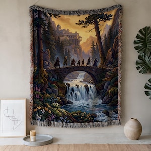 Puede incluir: Tapiz tejido que representa un paisaje de fantasía con un puente de piedra sobre una cascada. Figuras caminan por el puente hacia un castillo en la distancia. La obra de arte utiliza tonos de verde, marrón y azul, con un borde con flecos.
