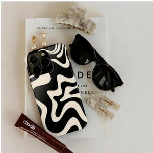 May include: A collection of accessories including a black and white swirl phone case, sunglasses, marble-patterned hair clips, and a tube of lip product. A book with the text "Stuffed with listings and" is visible.