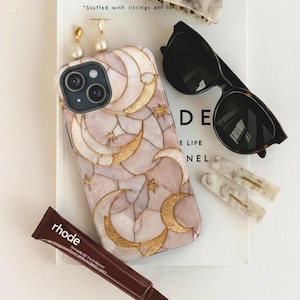 May include: An assortment of accessories including a phone case with a celestial design, sunglasses, hair clips, earrings, and lip balm. The phone case has gold moons and stars on a pink background.