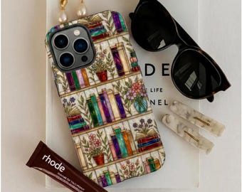 Op de afbeelding: Een smartphonehoesje met een kleurrijke boekenplankillustratie met gestapelde boeken en potplanten. Accessoires zijn onder meer een zwarte zonnebril, twee pareloorbellen, drie haarclips met marmerpatroon en een bruine tube met het label rhode.
