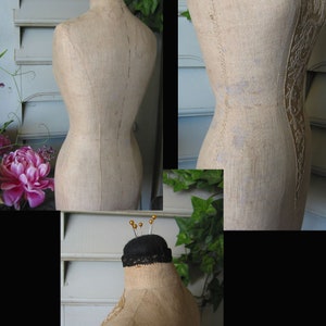 May include: A vintage, beige fabric dress form with a black fabric head and gold pins. The dress form has a seam down the center front and back, and a decorative design on the side.