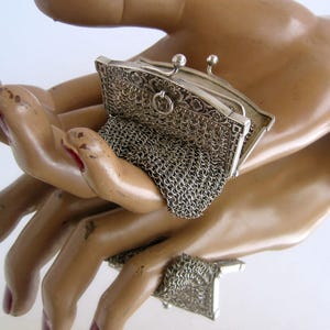 Könnte beinhalten: Eine silberne Netzgeldbörse mit einem Scharnierverschluss und einem verzierten Blumendesign. Die Börse ist geöffnet und das Netz ist sichtbar.