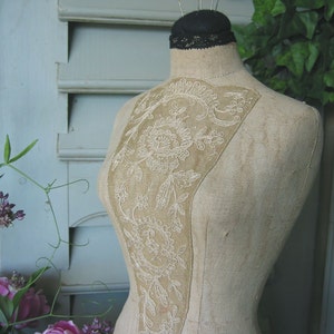 May include: A vintage fabric dress form with a delicate white lace design on the bodice. The form is made of a beige fabric and has a simple, classic design.
