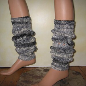 Op de afbeelding: Een paar grijze en witte gebreide beenwarmers met een textuurpatroon. De beenwarmers zijn aan de boven- en onderkant gerimpeld, waardoor een gerimpelde look ontstaat.