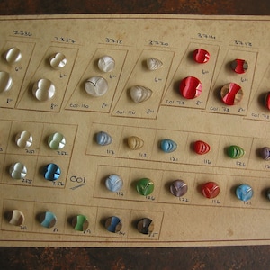 May include: A card with a grid of various buttons in different colours and shapes. The buttons are labelled with numbers and some have colour codes. The card is made of cardboard and has a brown background.
