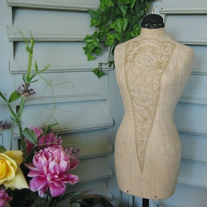 May include: A vintage dress form with a lace overlay, standing on a wooden base. The dress form is made of a beige fabric and has a delicate, floral design. The lace overlay is white and has a delicate, floral design. The dress form is standing on a wooden base.