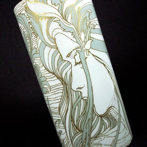 Op de afbeelding: Een witte keramische vaas met een gestileerd bloemenontwerp in tinten groen en goud. Het ontwerp toont een vrouwen gezicht en golvend haar.