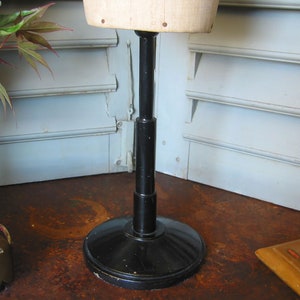 May include: A black adjustable stand with a round base for a dress form. The stand is made of metal and has a black finish.