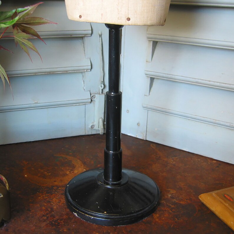 May include: A black adjustable stand with a round base for a dress form. The stand is made of metal and has a black finish.