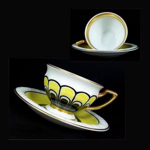 May include: A white teacup and saucer with a yellow, black and gold geometric design. The cup has a gold rim and the saucer has a gold band around the edge.