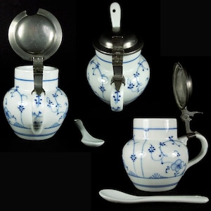 Può includere: Un creamer in porcellana bianca con un motivo floreale blu e un coperchio e un manico in peltro. Il creamer ha un piccolo beccuccio e un corpo rotondo. Viene fornito con un piccolo cucchiaio in porcellana bianca.