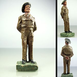 May include: A painted toy soldier figurine wearing a brown uniform and a black beret. The figurine is standing on a green base.