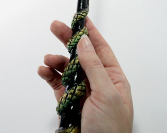 Pode incluir: Uma varinha preta com um design de cobra verde e dourada enrolado ao redor.