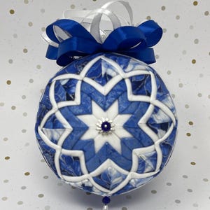 May include: Blue and white fabric Christmas ornament with a star design and a blue ribbon bow.