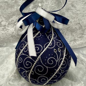 May include: A navy blue Christmas ornament with a silver and white swirl design. The ornament is decorated with navy blue and white ribbons. A festive decoration for the holiday season.