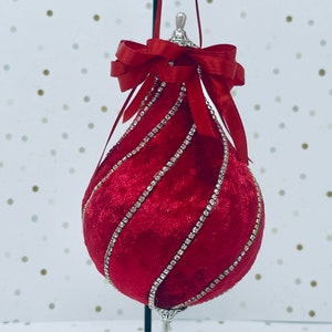 May include: A red velvet Christmas ornament with a swirl design and silver rhinestones. The ornament has a silver top and a red velvet bow.
