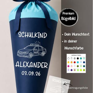 Könnte beinhalten: Eine dunkelblaue Schultüte mit hellblauem Stoffabschluss und dunkelblauer Schleife. Die Tüte zeigt den weißen Schriftzug SCHULKIND, ALEXANDER und 03.09.26 sowie eine weiße Grafik eines Polizeiautos. Enthält eine Übertragungsfolie für das Bügelbild.