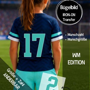 Könnte beinhalten: Ein dunkelblaues Kurzarmshirt mit Chevron-Muster, das auf der Rückseite die Zahl 17 in Hellblau zeigt. Das Shirt hat hellblau-weiß gestreifte Ärmelbündchen. Der Text umfasst Bügelbild, IRON-ON Transfer, WM EDITION und Übertragungsfolie.