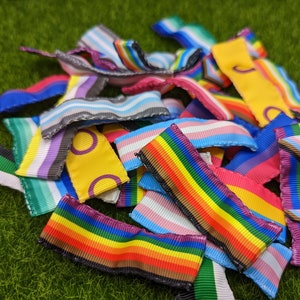May include: A collection of colorful rainbow ribbon scraps with various patterns and designs. The ribbons are made of satin and have a smooth texture.