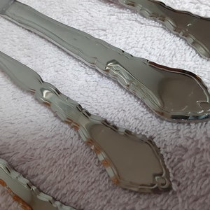 May include: Four silver flatware pieces with ornate designs on a white towel.