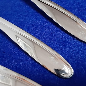 May include: Three silver spoons with polished, reflective surfaces. The spoons are arranged on a blue background.